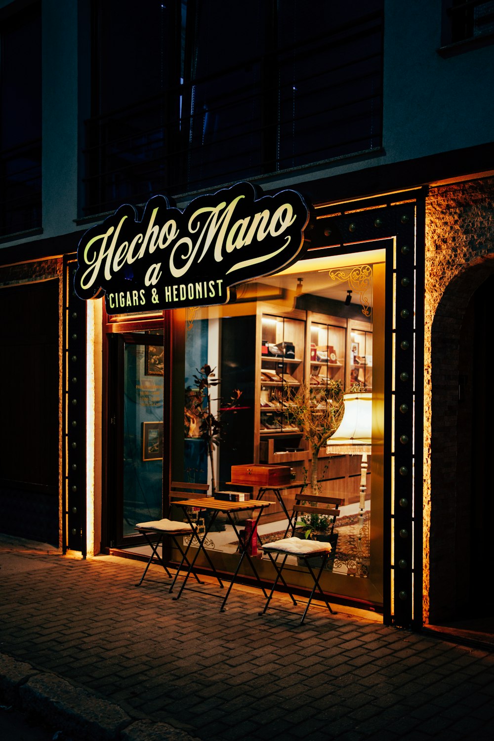 a store front at night with a lit up table and chairs