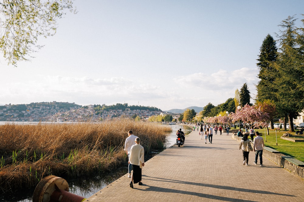 a group of people walking down a sidewalk next to a river