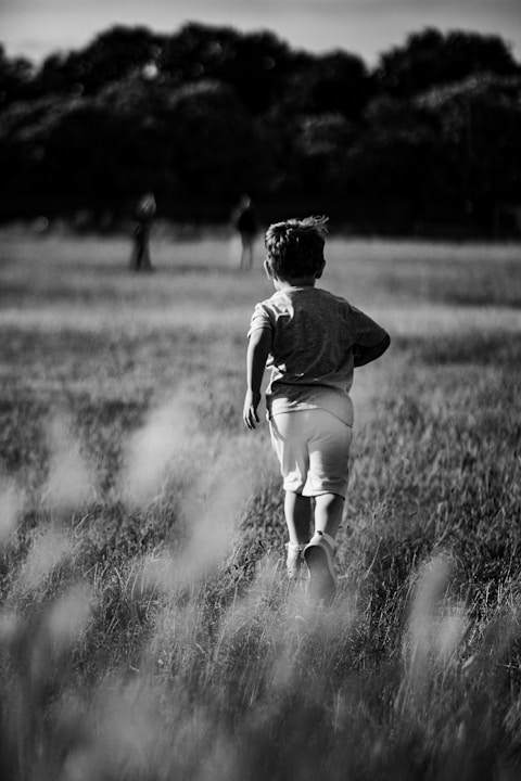 a little boy running through a field of tall grass