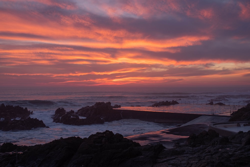 the sun is setting over the ocean and rocks