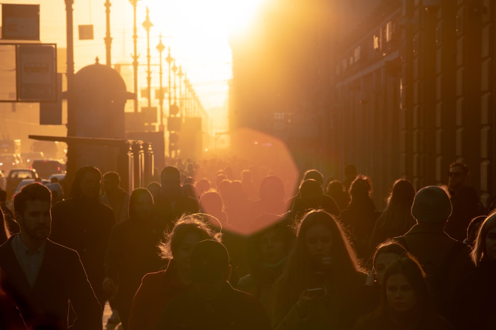 a crowd of people walking down a street at sunset