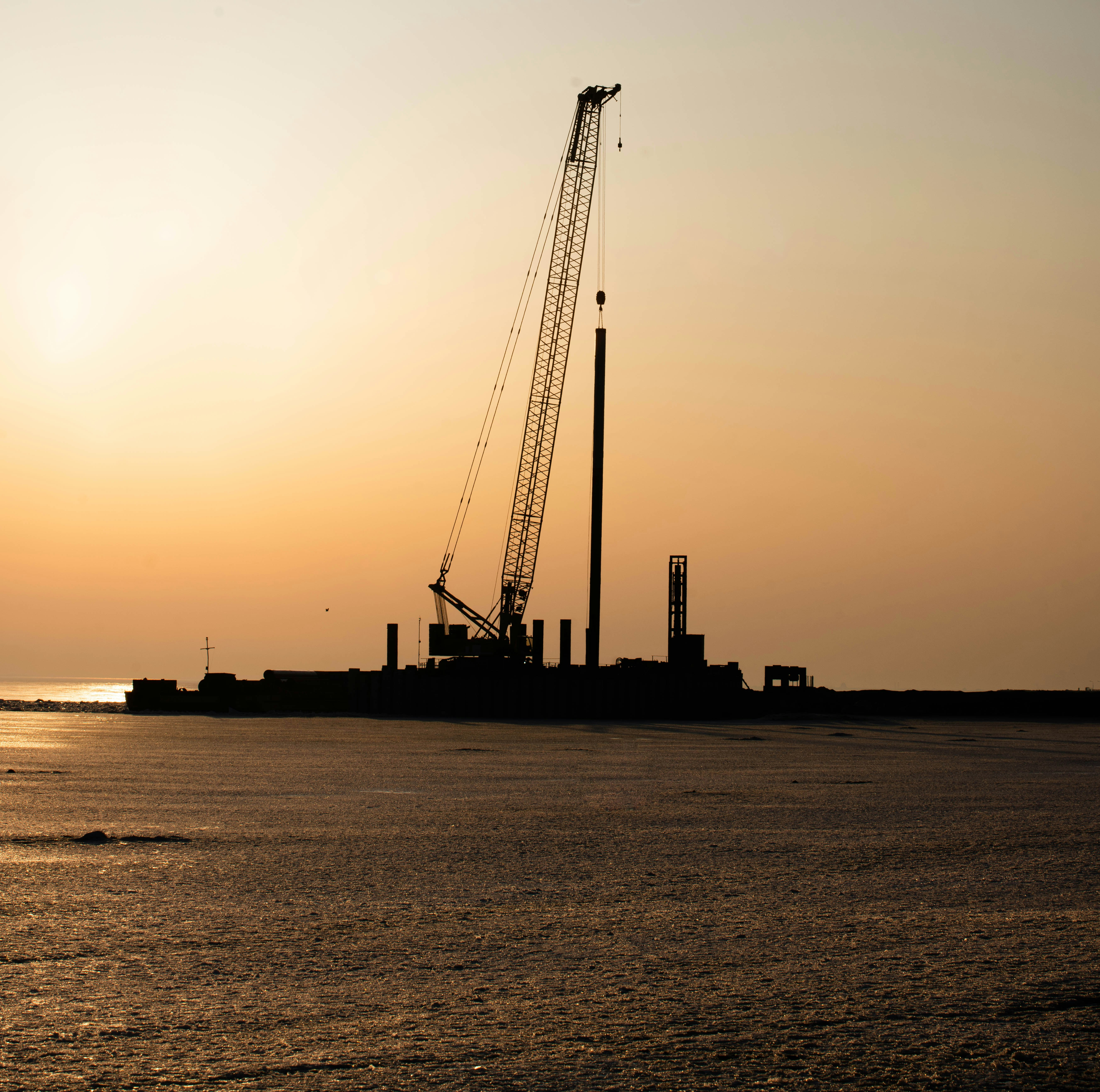 Silhouette of an offshore drilling site at sunrise, highlighting early-stage operations.