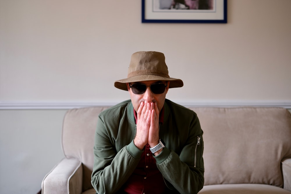 a man in a hat and sunglasses sitting on a couch