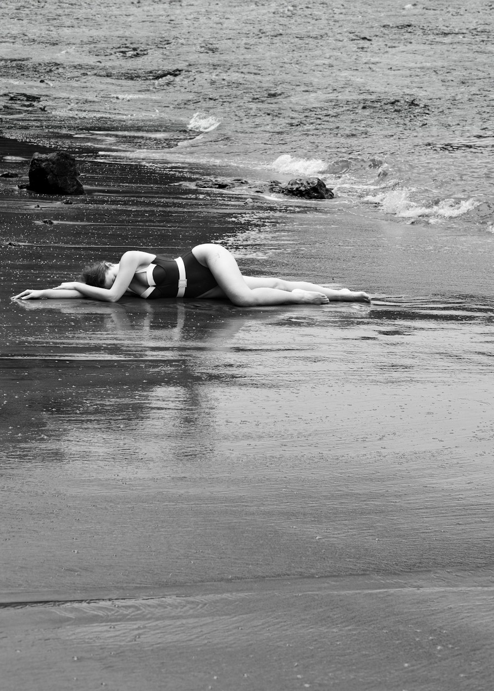 a woman laying on top of a beach next to the ocean