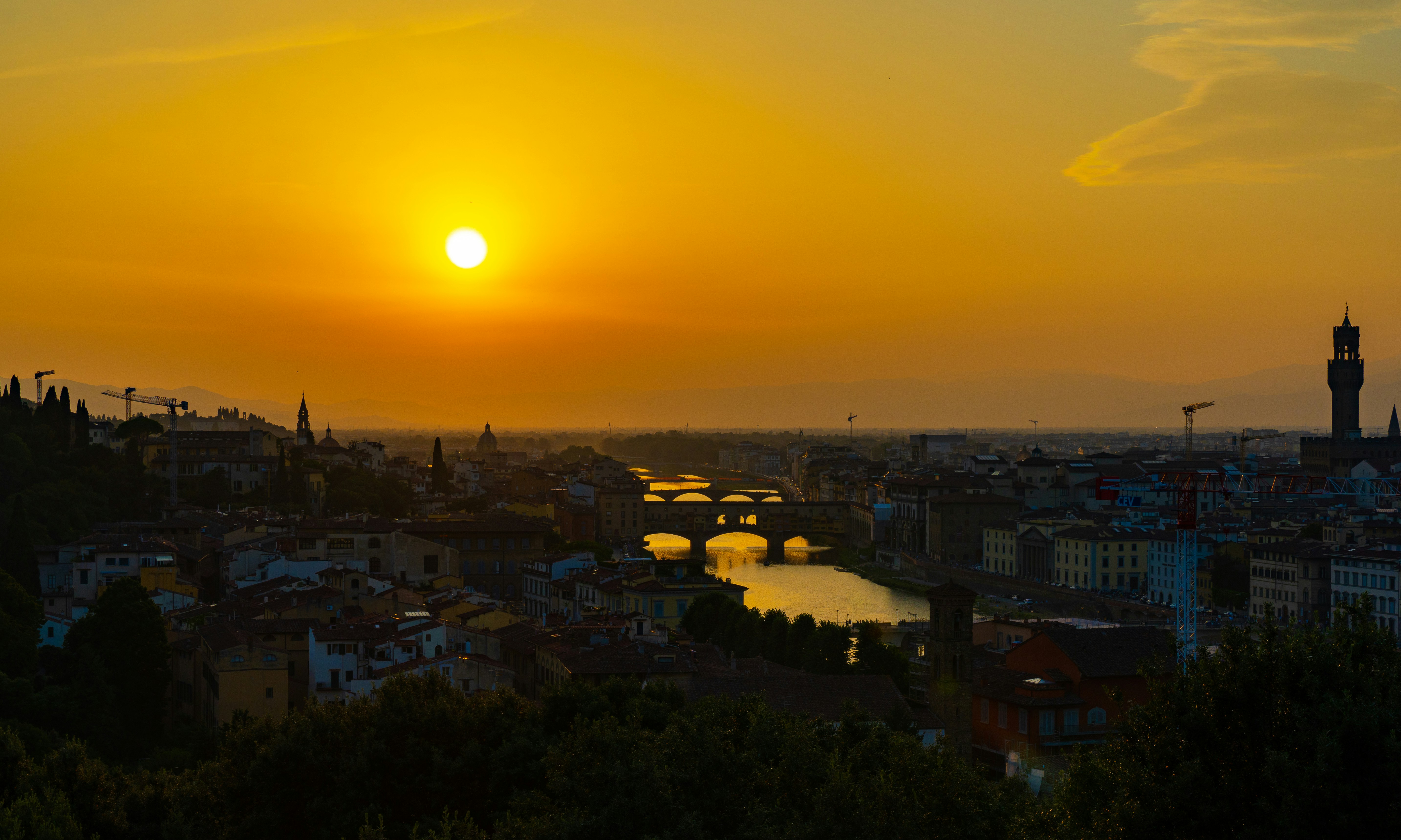 the sun is setting over a city with a bridge
