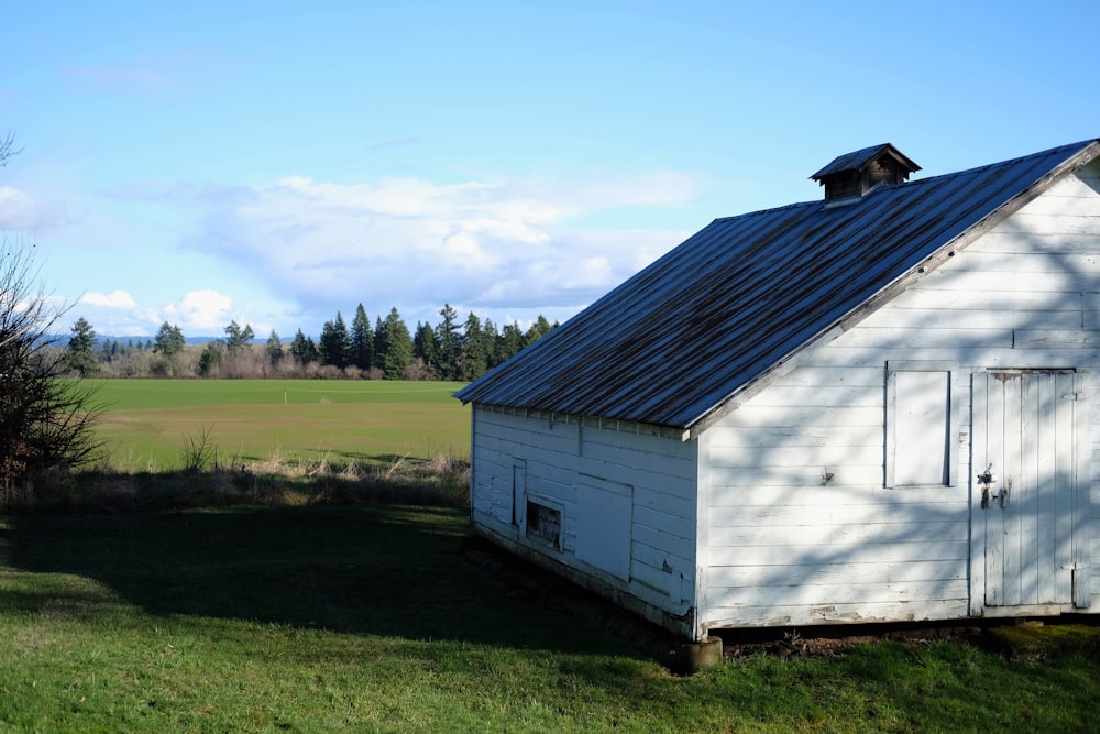 um celeiro branco com um telhado de metal em um campo