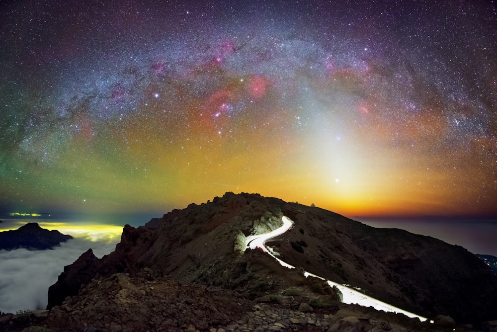 a mountain with a road going through it under a night sky filled with stars