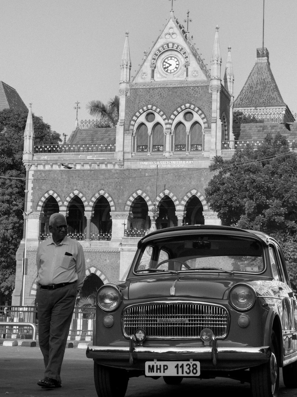 a black and white photo of a man standing next to a car