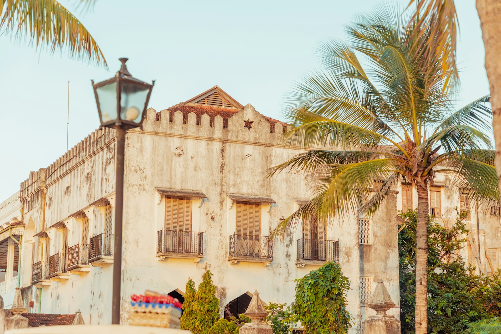 Weathered coral-stone facade with shuttered balconies, a palm and an old street lamp in Stone Town