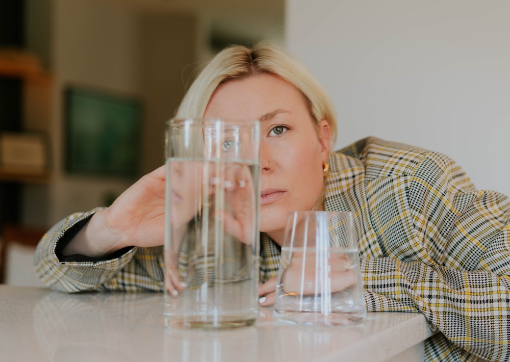 una mujer apoyada en una mesa con varios vasos de agua