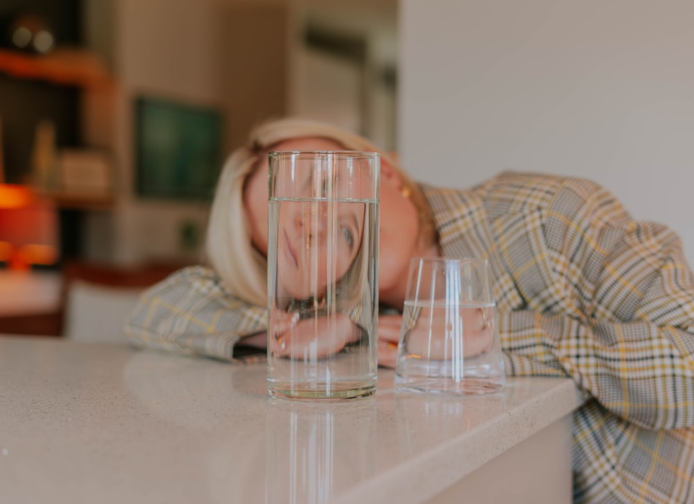 a woman laying her head on a counter next to a glass of water