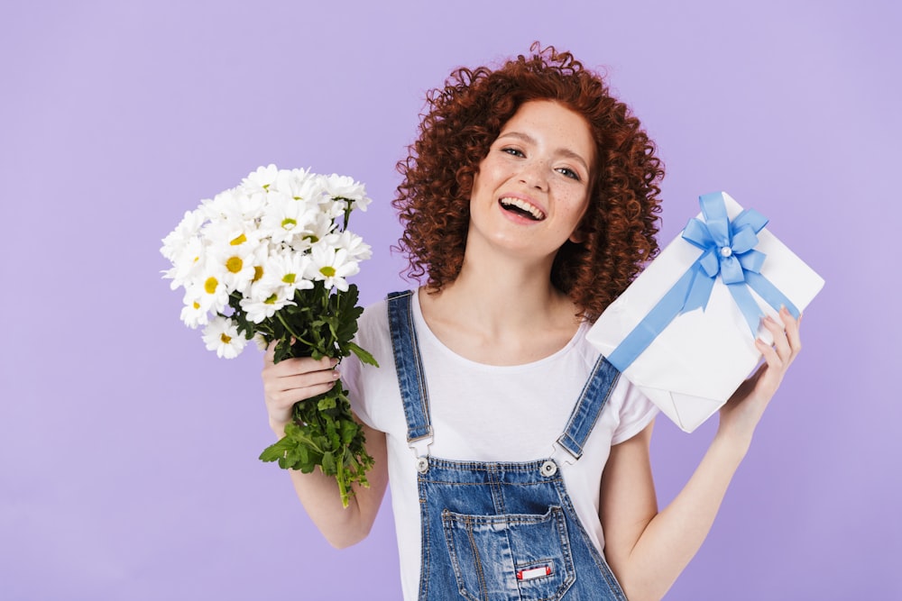 a woman holding a bouquet of daisies and a gift