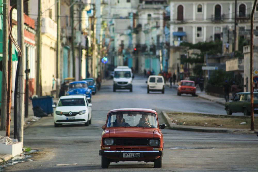 a red car driving down a street next to tall buildings