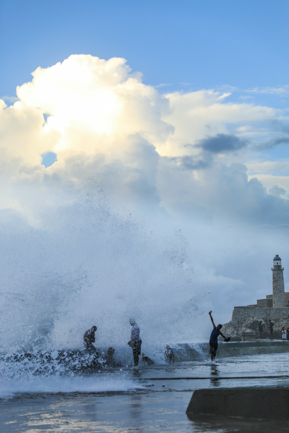 a group of people standing on top of a beach next to a large wave