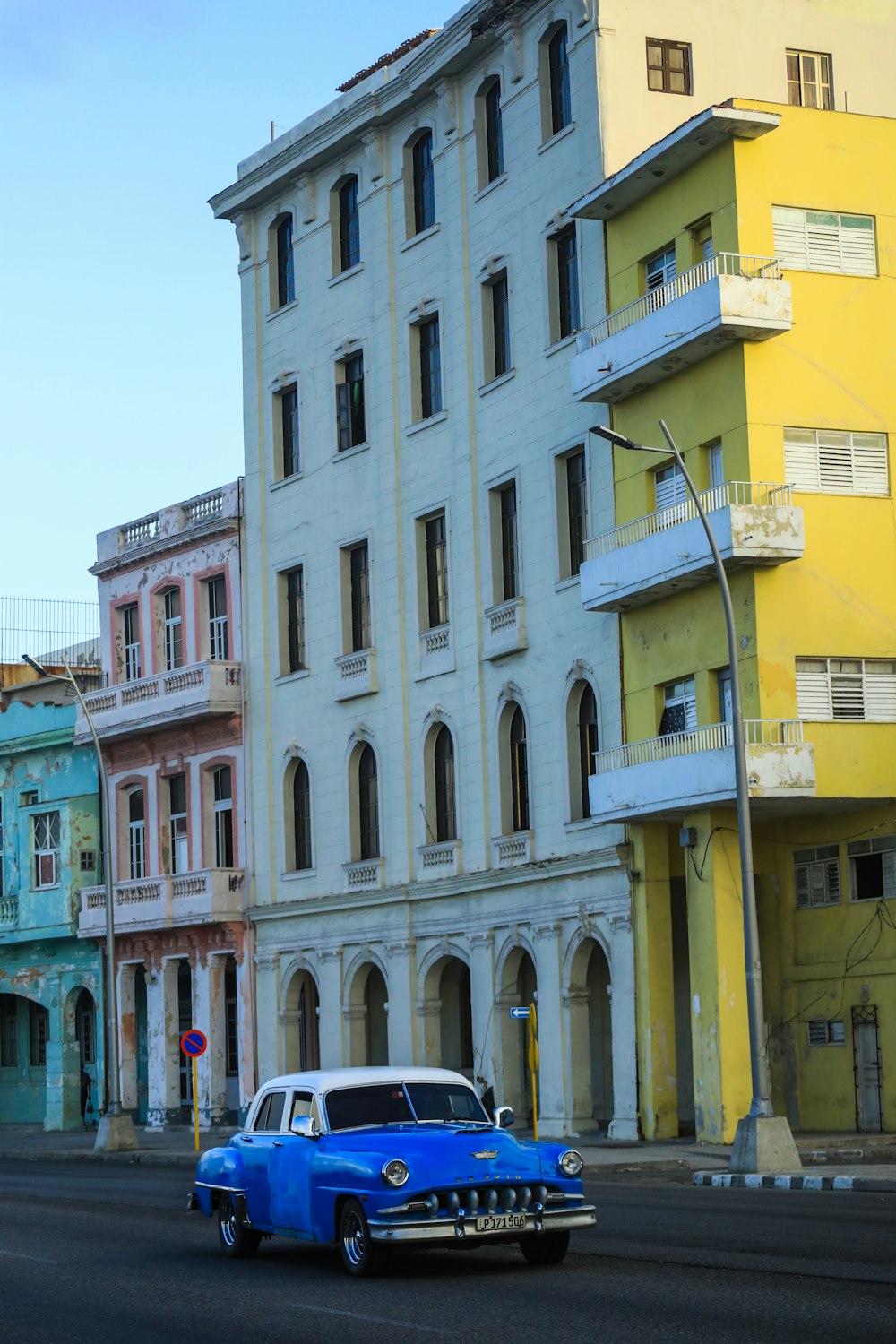 a blue car driving down a street next to tall buildings