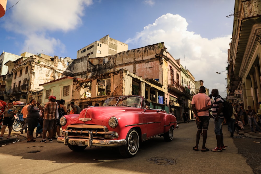 a group of people standing around a red car