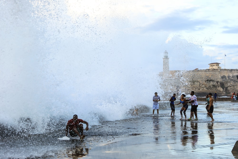 a group of people standing on top of a beach next to a wave