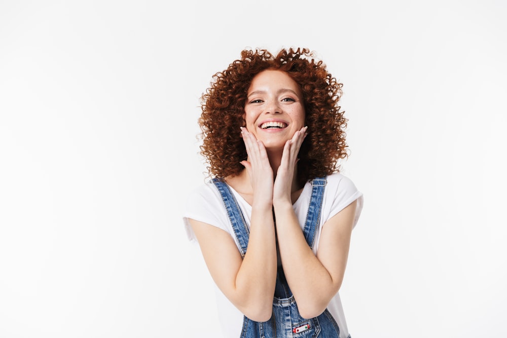 a woman with curly hair and overalls posing for a picture