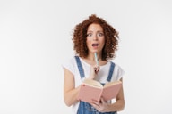 a woman in overalls holding a book and a pencil