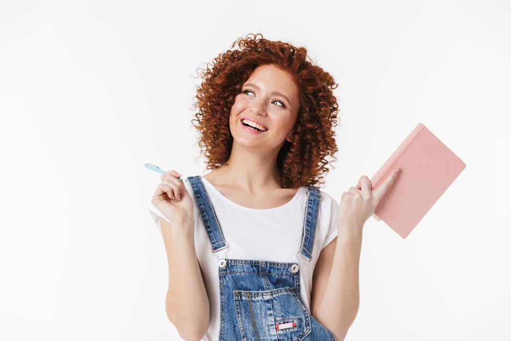 a woman with curly hair is holding a notebook and a toothbrush