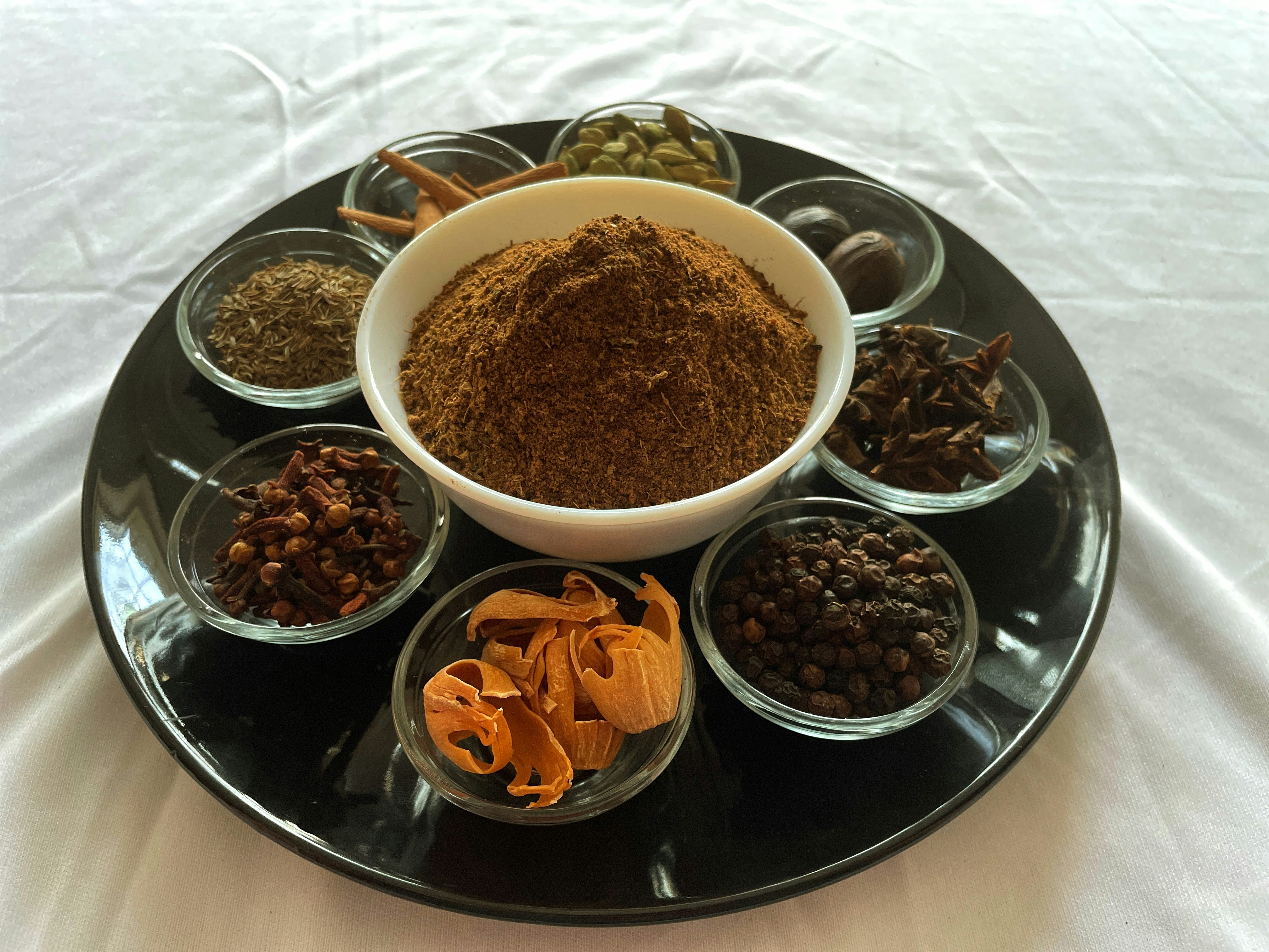 Colorful assortment of aromatic spices in small bowls on a dark surface