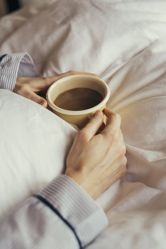 a person laying in bed holding a cup of coffee
