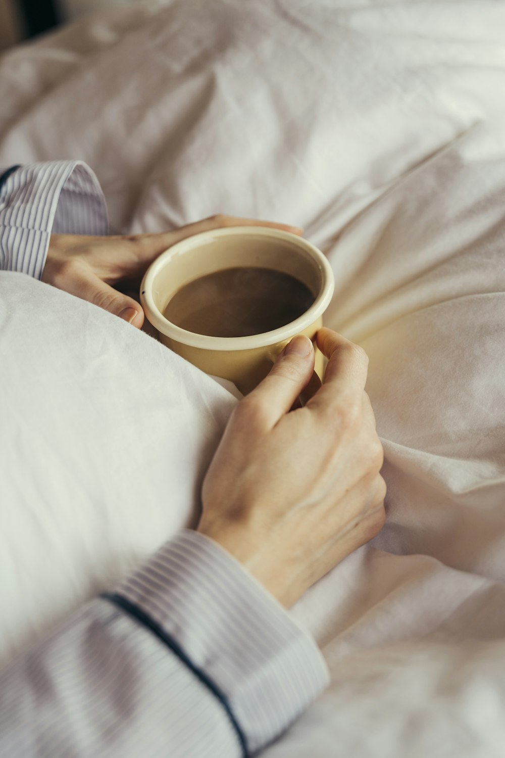 a person laying in bed holding a cup of coffee