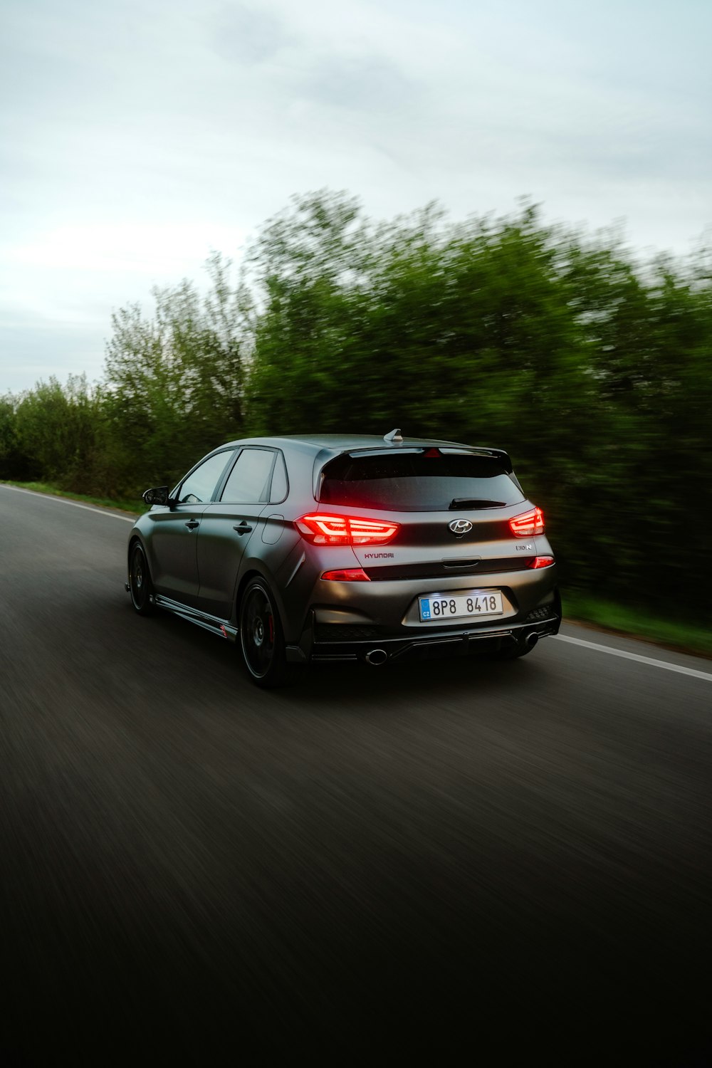 a black car driving down a road next to a forest