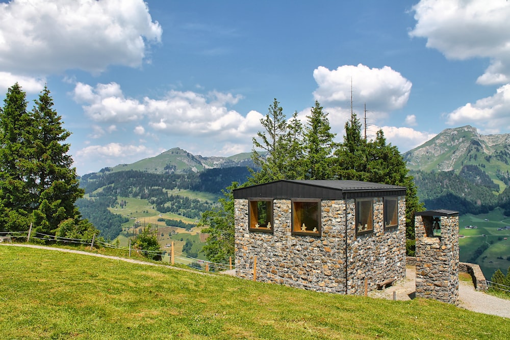 a small building on a grassy hill with mountains in the background