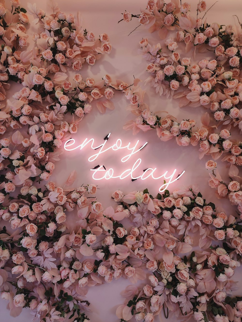 a neon sign that says enjoy today surrounded by flowers