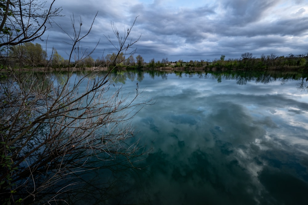 a body of water surrounded by trees under a cloudy sky