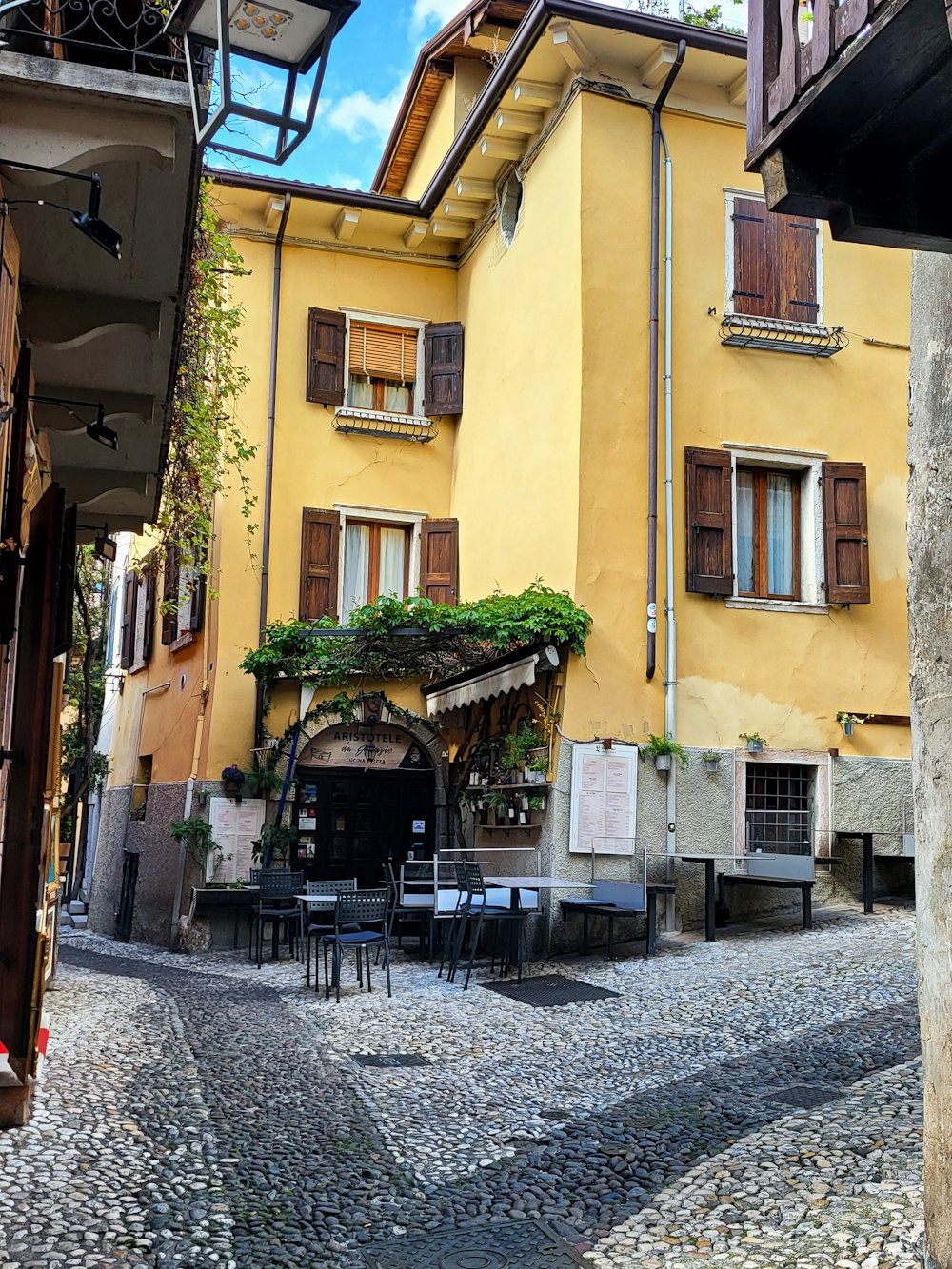 a cobblestone street with tables and chairs in front of a yellow building