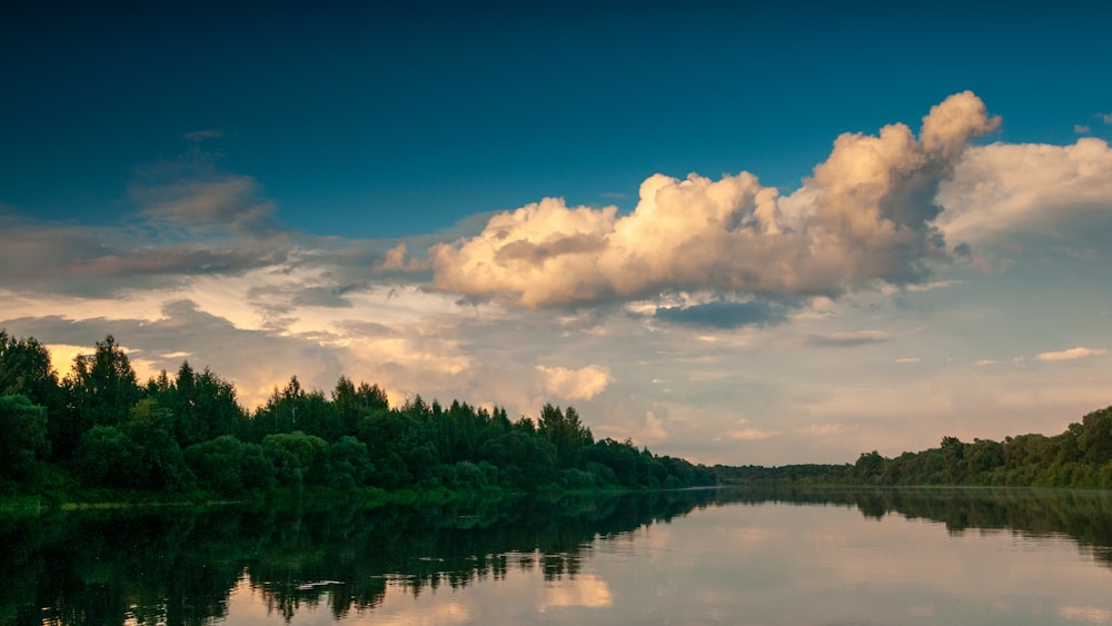 a body of water surrounded by trees under a cloudy sky