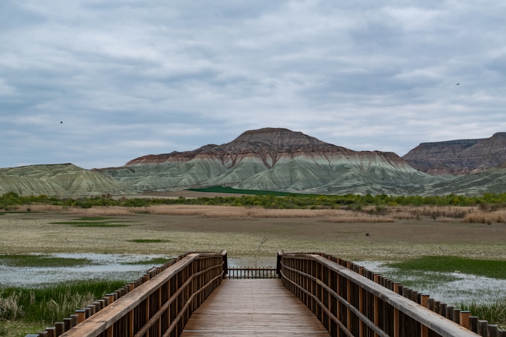 a wooden bridge over a river with mountains in the background