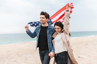 a man and woman walking on a beach holding an american flag