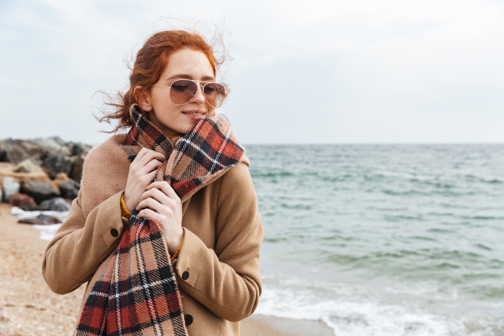 a woman standing on a beach with a plaid scarf around her neck