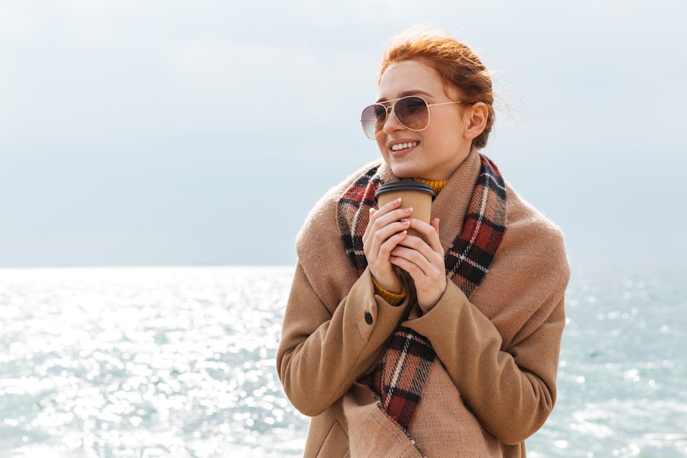 a woman standing on a beach holding a cup of coffee