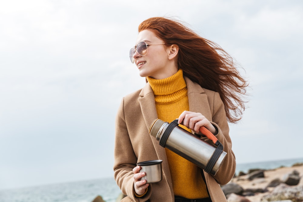 a woman holding a coffee cup and looking at the ocean
