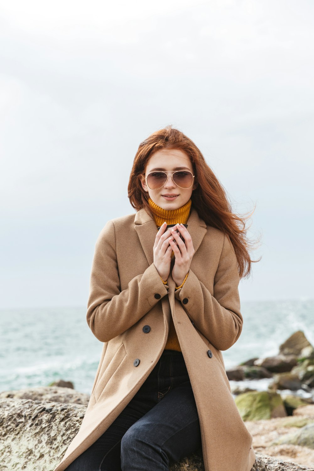 a woman sitting on a rock near the ocean