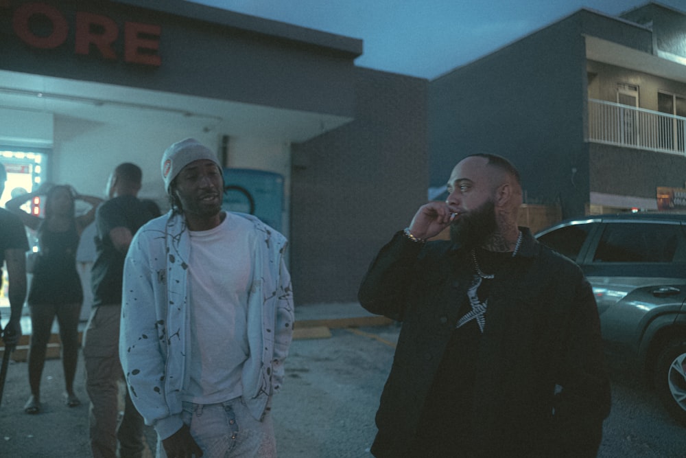 two men standing in front of a store talking on their cell phones