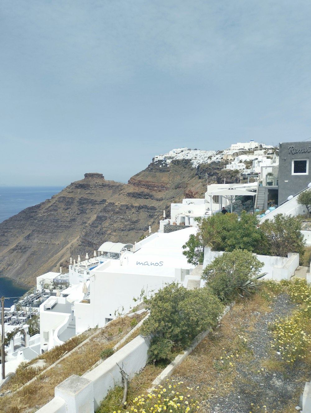 a view of a hillside with white buildings and a body of water in the distance
