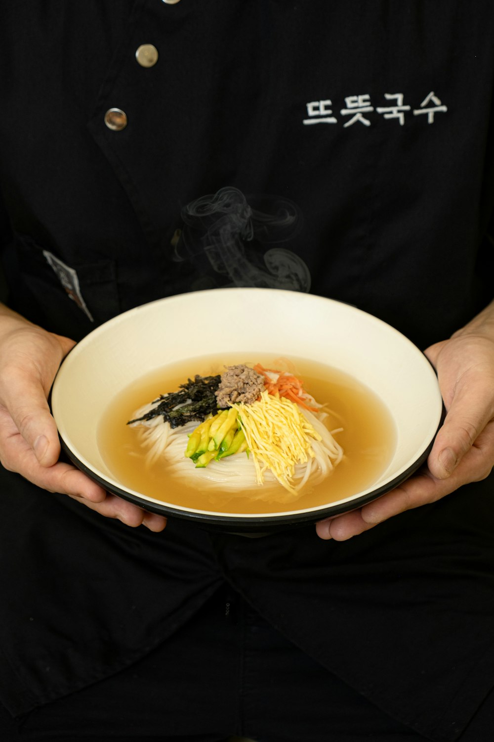 a person holding a bowl of soup with noodles