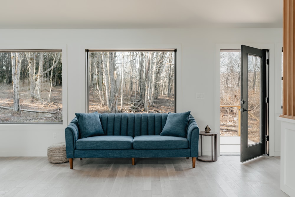 un sofá azul sentado en una sala de estar junto a dos ventanas