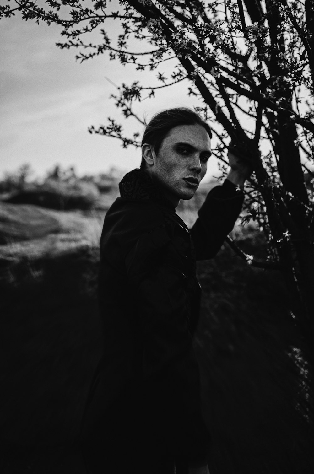 a man standing next to a tree in a black and white photo