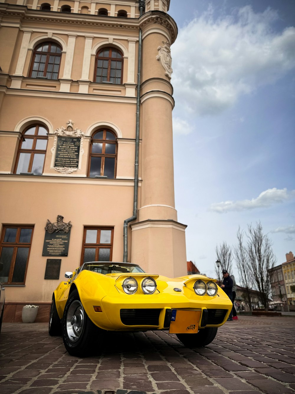 a yellow sports car parked in front of a tall building