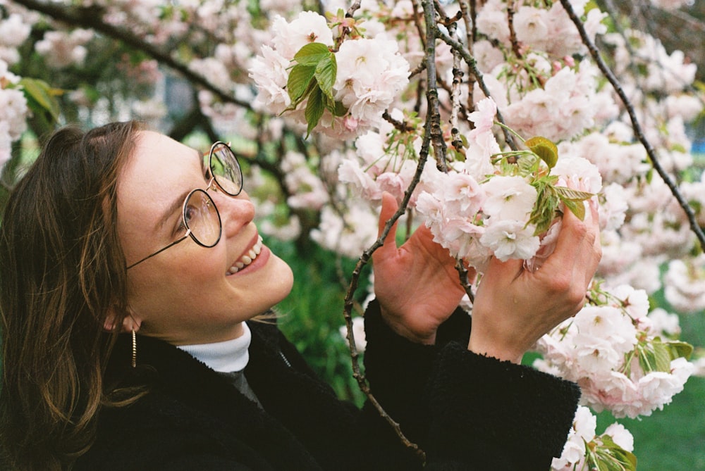 a woman in glasses is smiling and holding a branch of a cherry blossom tree