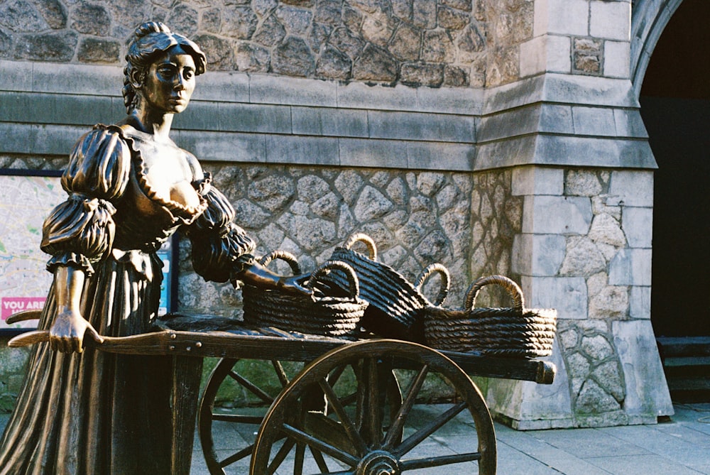 uma estátua de uma senhora empurrando um carrinho com cestos sobre ele