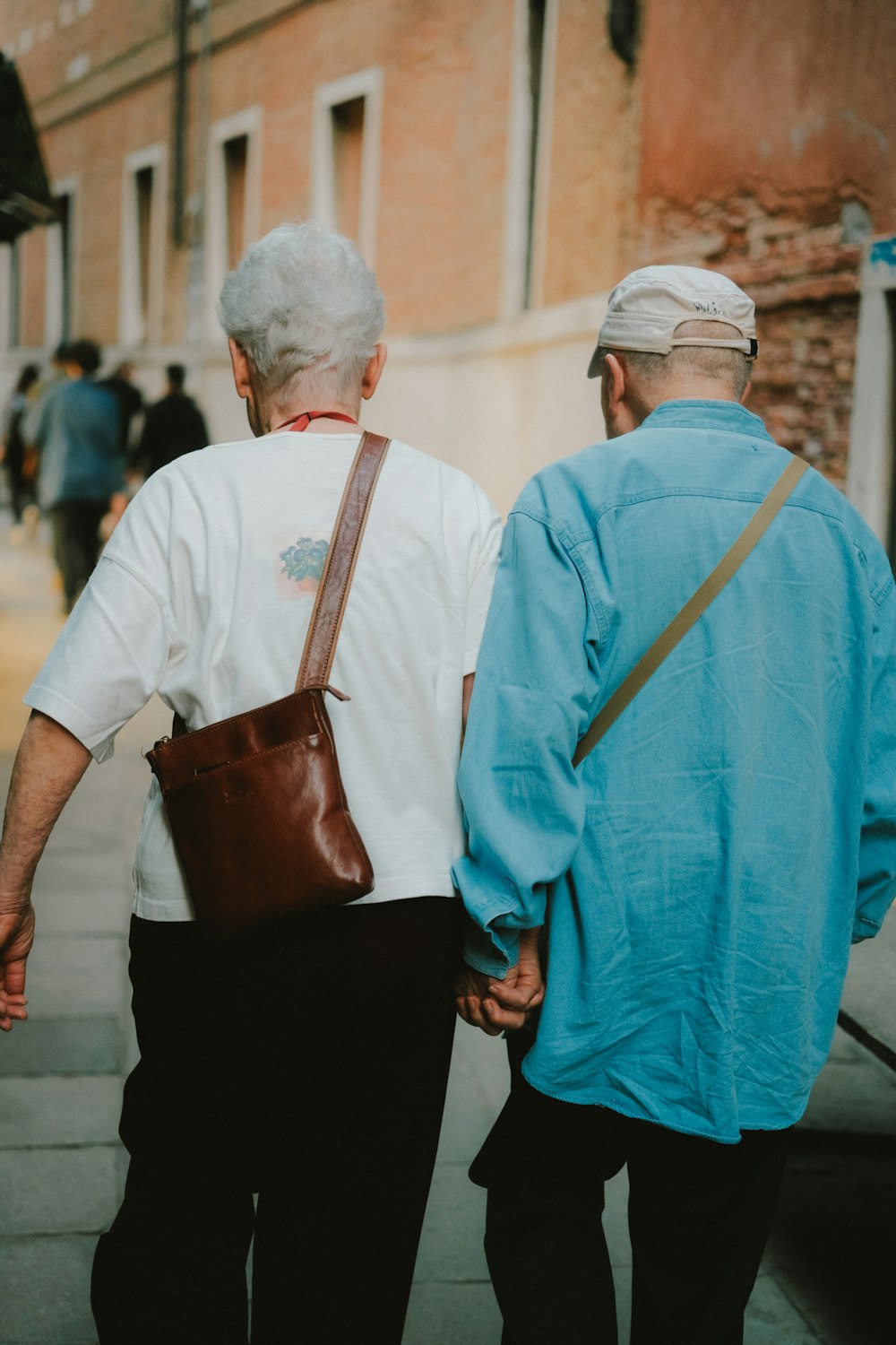 two elderly people walking down a street holding hands
