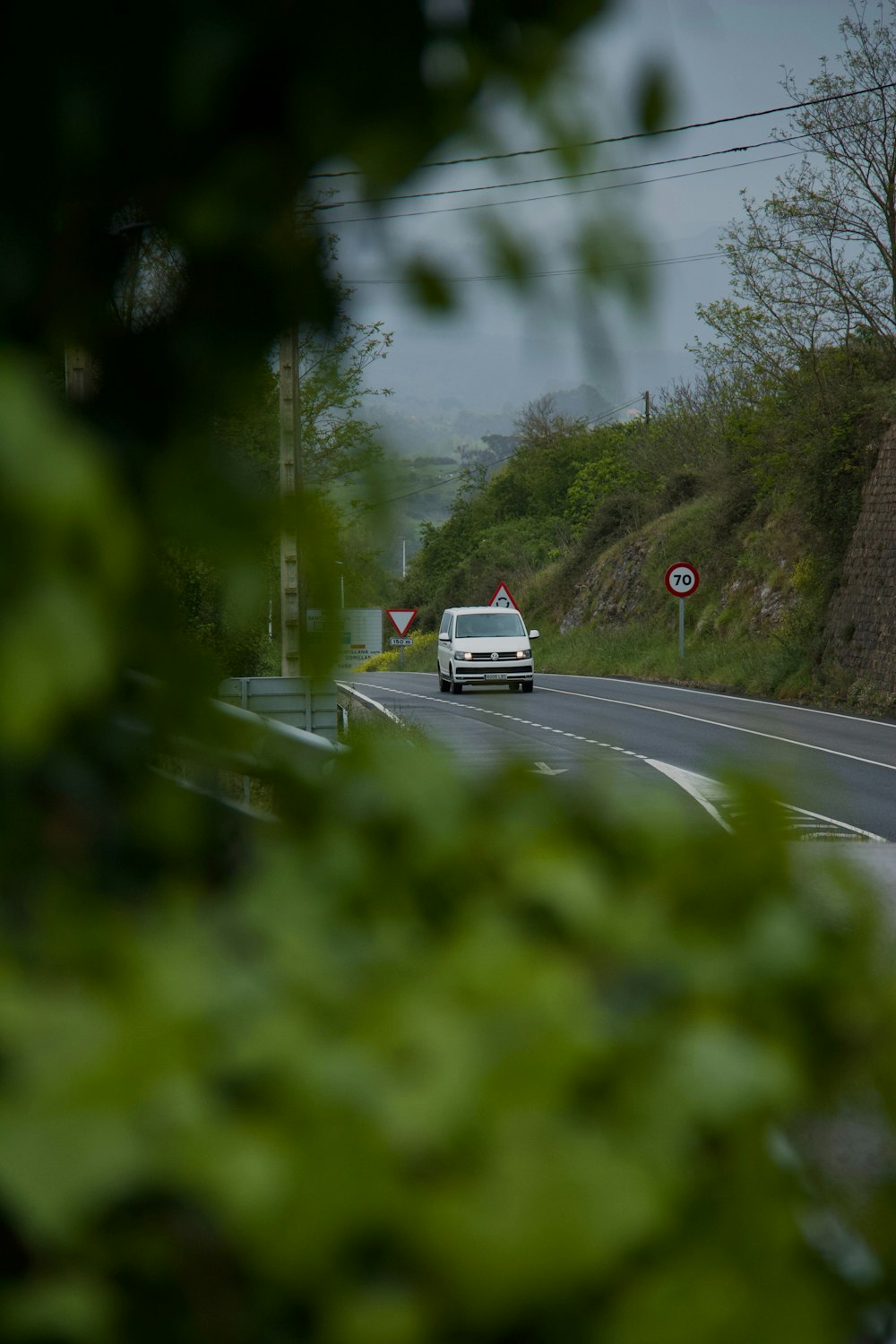 a white truck driving down a road next to a lush green hillside