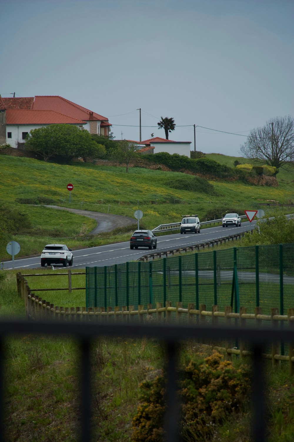 a group of cars driving down a road next to a lush green hillside